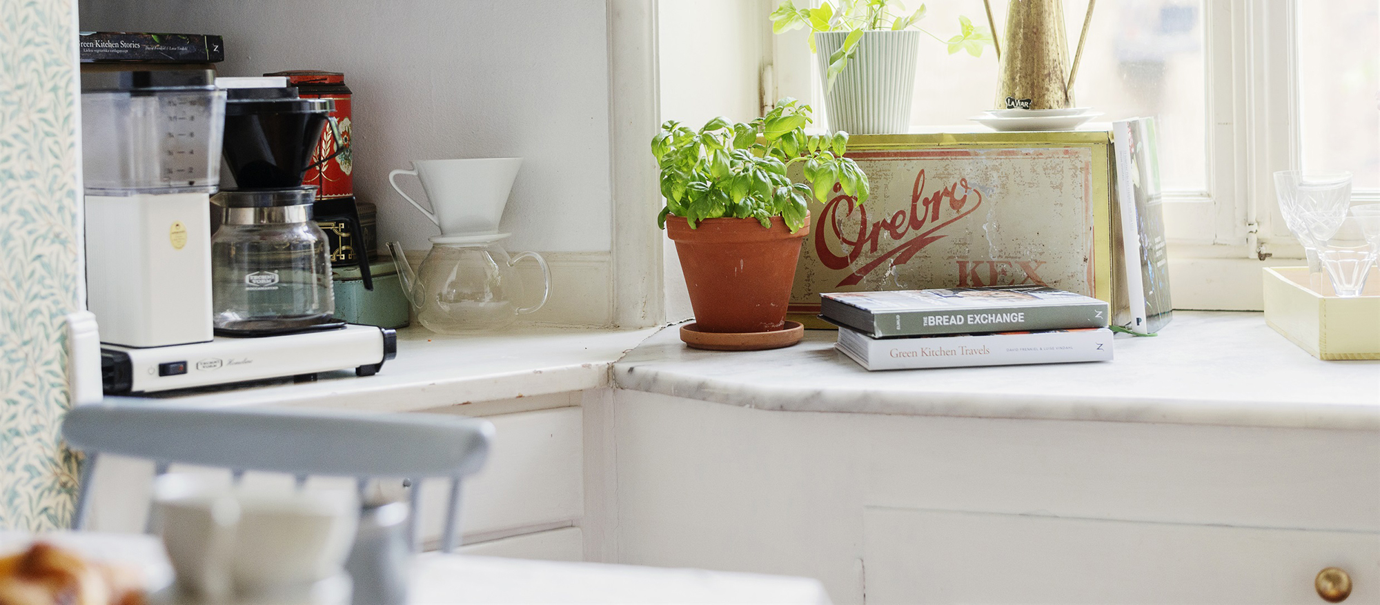 Dekorationsbild. En vit köksbänk med kaffebryggare och krukväxt framför ett soligt fönster