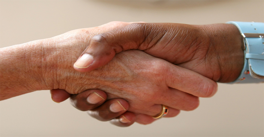 En vit kvinnas hand i en färgad persons hand.