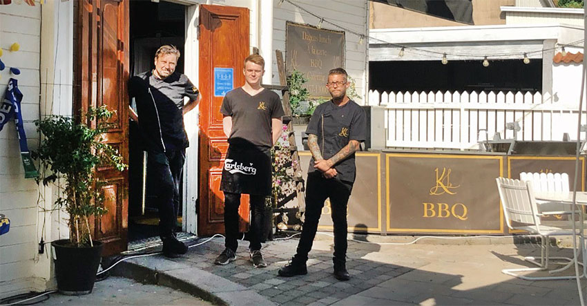 Tre unga män som står i en dörröppning vid en innergård till en restaurang.