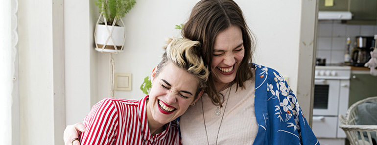 två skrattande kvinnor håller om varandra i en ljus lägenhet
