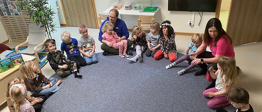 barn och vuxna sitter i en ring på en grå matta