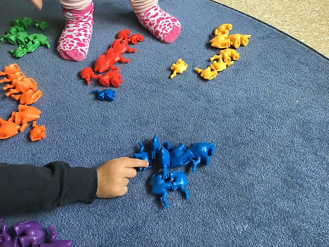 leksaker i olika färger ligger sorterade på en blå matta, små barnfötter och barnhänder syns med i bilden