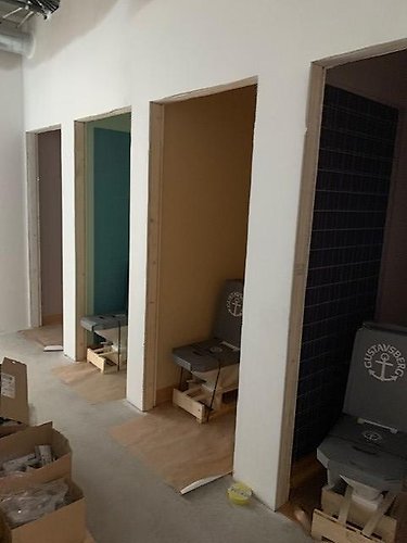 Byggbild med ouppackade toalettstolar som står i dörröppningen till respektive toalett