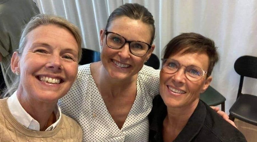 Tre kvinnor ler in i kameran